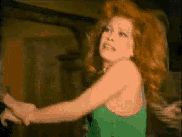 a woman with red hair is wearing a green tank top and has her arms outstretched .