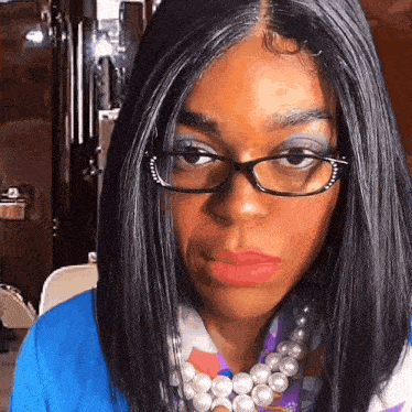 a woman wearing glasses and a pearl necklace looks serious