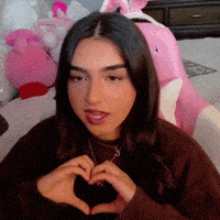 a woman making a heart shape with her hands in front of a pink chair