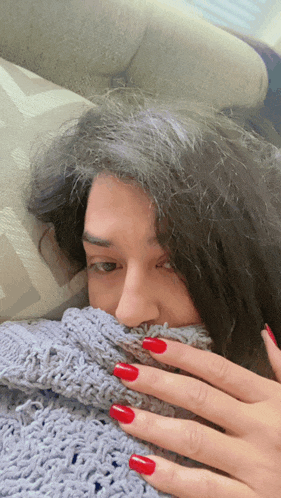 a woman with red nails is covering her face with a grey blanket