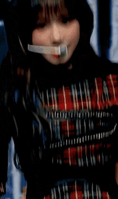 a close up of a woman wearing a plaid top with a microphone in her mouth