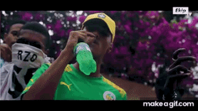 a man wearing a green shirt and a yellow hat drinks from a green bottle