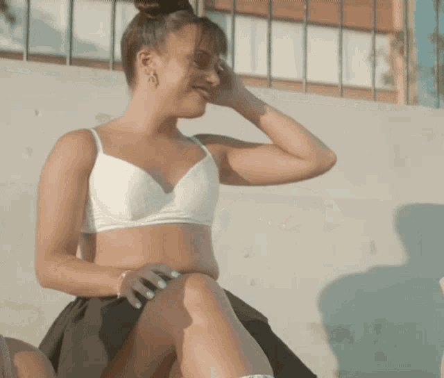 a woman in a white bra and black skirt is sitting on a ledge .