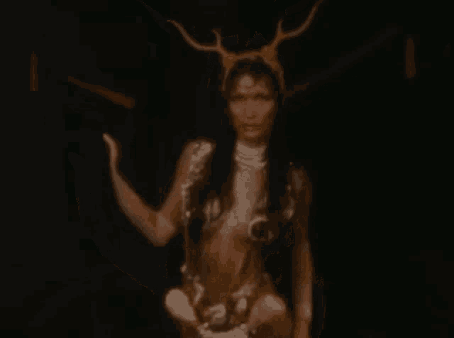 a woman in a costume with horns on her head is holding a snake in her hand .