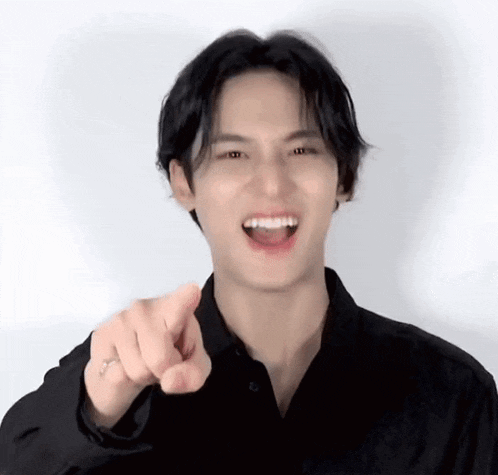 a young man wearing a black shirt is pointing at the camera .