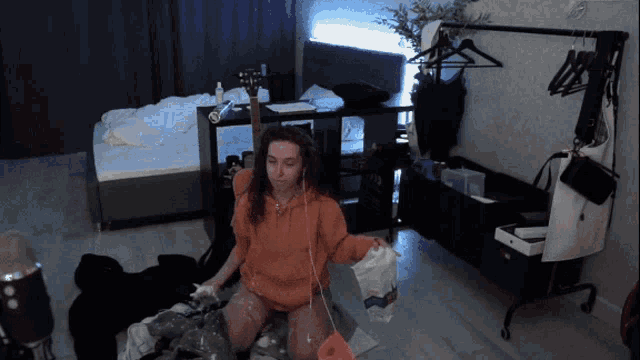 a woman in an orange hoodie sits on the floor holding a bag that says ' coca cola ' on it