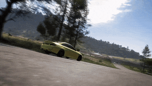 a yellow car driving down a road with trees in the background