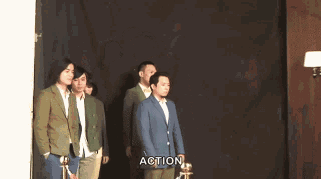 a group of men are standing in front of a black curtain and the word action is visible