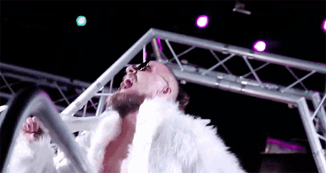 a man wearing a white fur coat and sunglasses is standing in front of a stage .