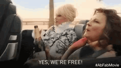 two women are sitting in a car and one of them is holding a bottle of champagne .
