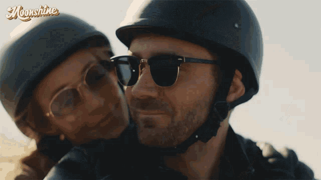 a man and a woman wearing helmets and sunglasses are smiling in front of a sign that says moonshine