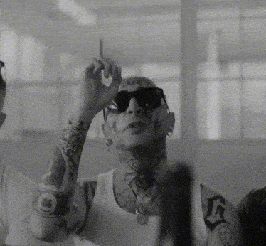 a black and white photo of a tattooed man wearing sunglasses and a white tank top