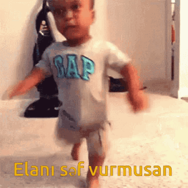 a baby wearing a gap shirt walks on the floor