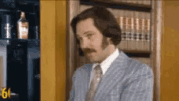 a man in a suit and tie is standing in front of a bookshelf with books on it .