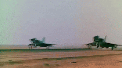 two fighter jets are taking off from a runway in a desert