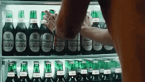 a person is reaching into a refrigerator filled with bottles of lager .