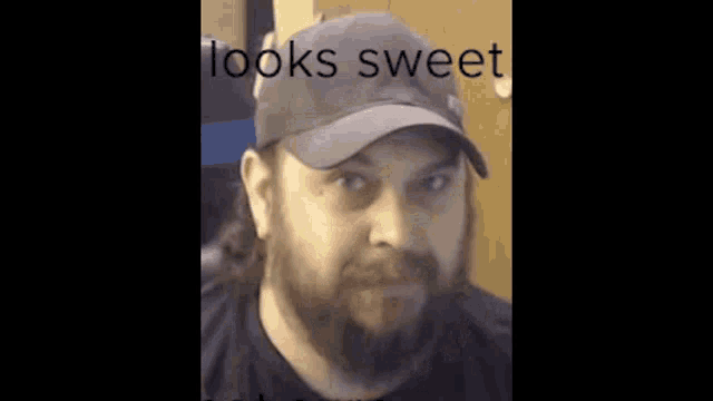 a man with a beard wearing a baseball cap and a black shirt is looking at the camera .