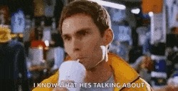 a man in a yellow jacket is talking on a cell phone while drinking a cup of coffee .
