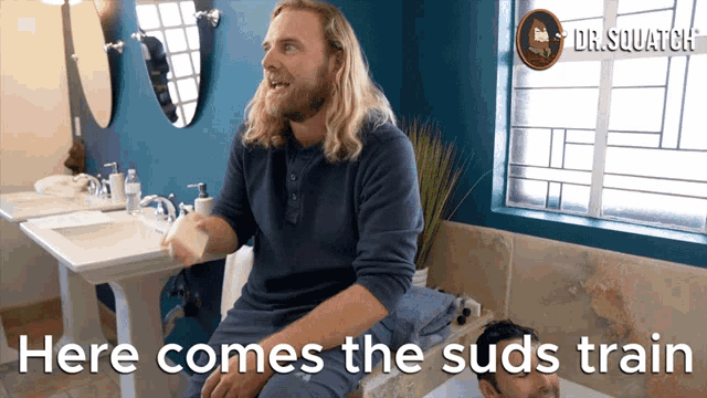 a man sitting in a bathroom with the words here comes the suds train on the bottom