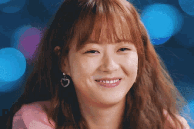 a close up of a woman wearing a pink shirt and heart shaped earrings