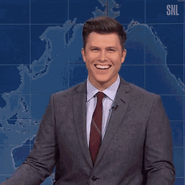 a man in a suit and tie is smiling in front of a snl logo
