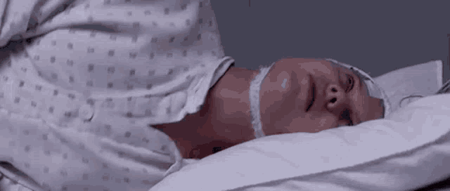 a woman in a hospital gown is laying in a hospital bed with a bandage on her head .