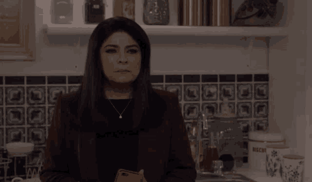 a woman in a kitchen holding a cell phone in front of a shelf that says sugar