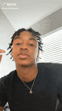 a young man with dreadlocks is wearing a black shirt and a gold necklace .