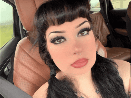 a woman with pigtails and a nose ring is sitting in the back seat of a car