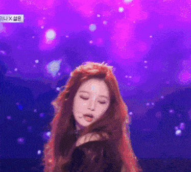 a woman with long red hair is standing in front of a purple background with the word x on it