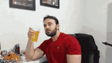 a man in a red shirt is holding a glass of beer in his hand