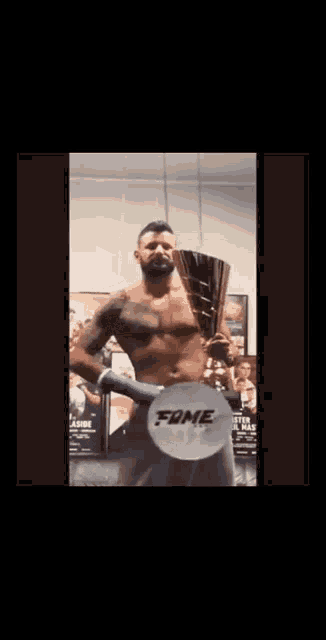a shirtless man is holding a trophy in front of a sign that says " fame "