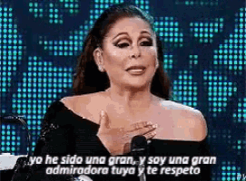 a woman in a black off the shoulder top is speaking into a microphone in front of a blue background .