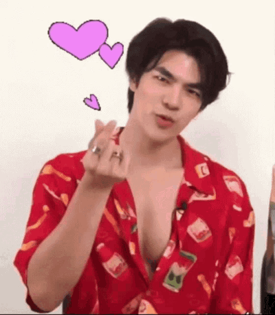 a young man in a red shirt is making a heart shape with his hand .