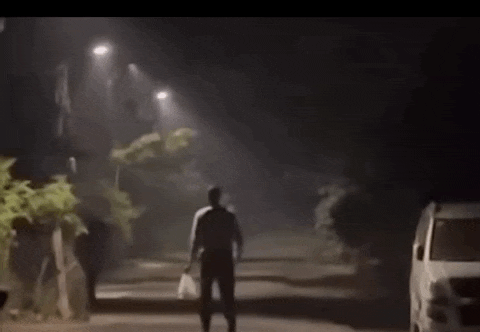 a man is running down a street at night while a car is parked on the side of the road .