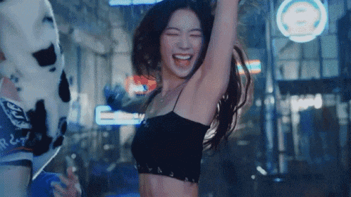 a woman in a black crop top is dancing with her arms in the air in a city .