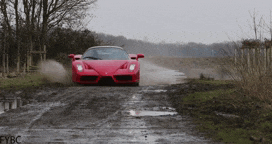 a red sports car is driving down a muddy dirt road