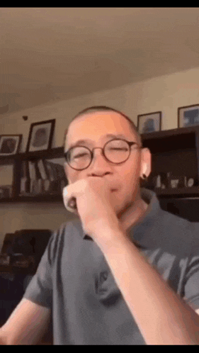 a man wearing glasses and a gray shirt is eating something .