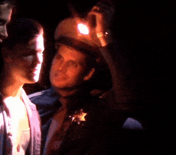 a man in a sheriff 's hat is holding a flashlight over his head