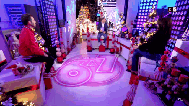 a man in a red jacket sits on a stool in front of a sign that says ' cb '