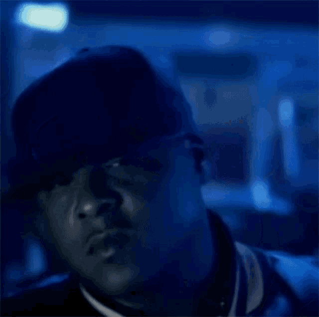 a man wearing a hat and a jacket is standing in a dark room with blue lights .