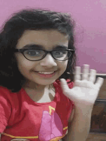 a young girl wearing glasses and a red shirt is smiling and waving