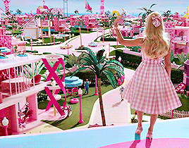 a barbie doll in a pink dress is standing in front of a barbie world .