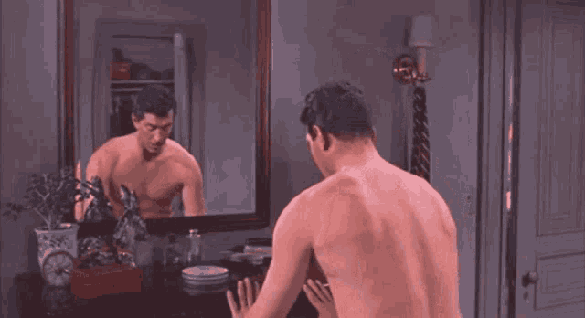 a man without a shirt is looking at himself in the mirror