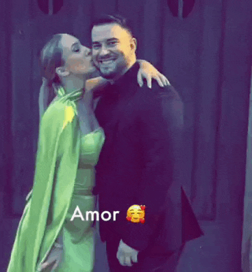 a woman in a green dress kisses a man on the cheek in front of a sign that says amor