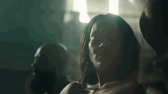 a woman without a shirt is dancing in a dark room with a man in the background .
