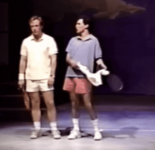 two men standing on a stage with tennis racquets