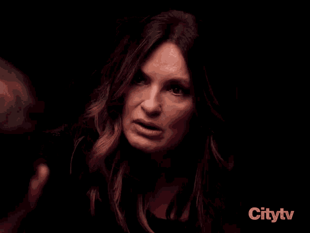 a woman is talking to a man in a dark room and covering her face with her hands .