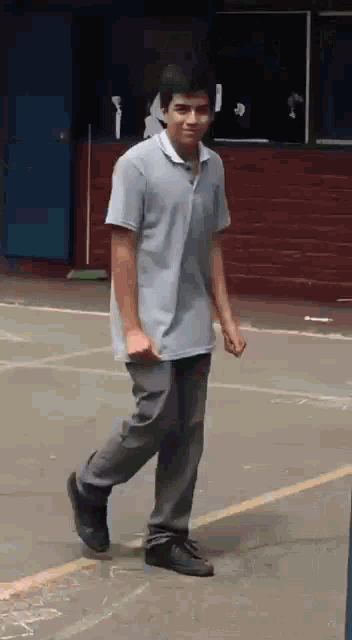a young man in a gray shirt and gray pants is walking on a concrete surface