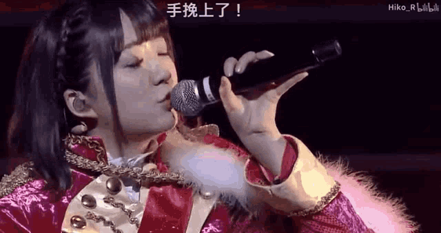 a woman is singing into a microphone with chinese writing on the screen behind her